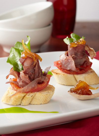Montaditos de carne oreada santandereana sobre pan francés, con cebollas caramelizadas, tomates confitados y rúgula