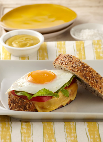 Sándwich de huevo frito, mostaza, queso holandés, pesto de albahaca y rodajas de tomate en pan de centeno y ajonjolí